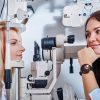 Sceptical optometrist is checking vision of young beautiful woman using special machine.