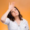 Closeup portrait annoyed tired middle aged woman placing back hand on forehead, tragedy of it all, woe is me, exaggerating isolated orange background. Negative emotion, facial expression, perception